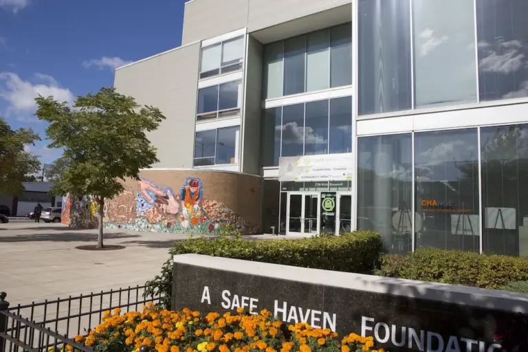 Glass-front A Safe Haven Foundation building with a colorful mural, trees, and orange marigolds in front