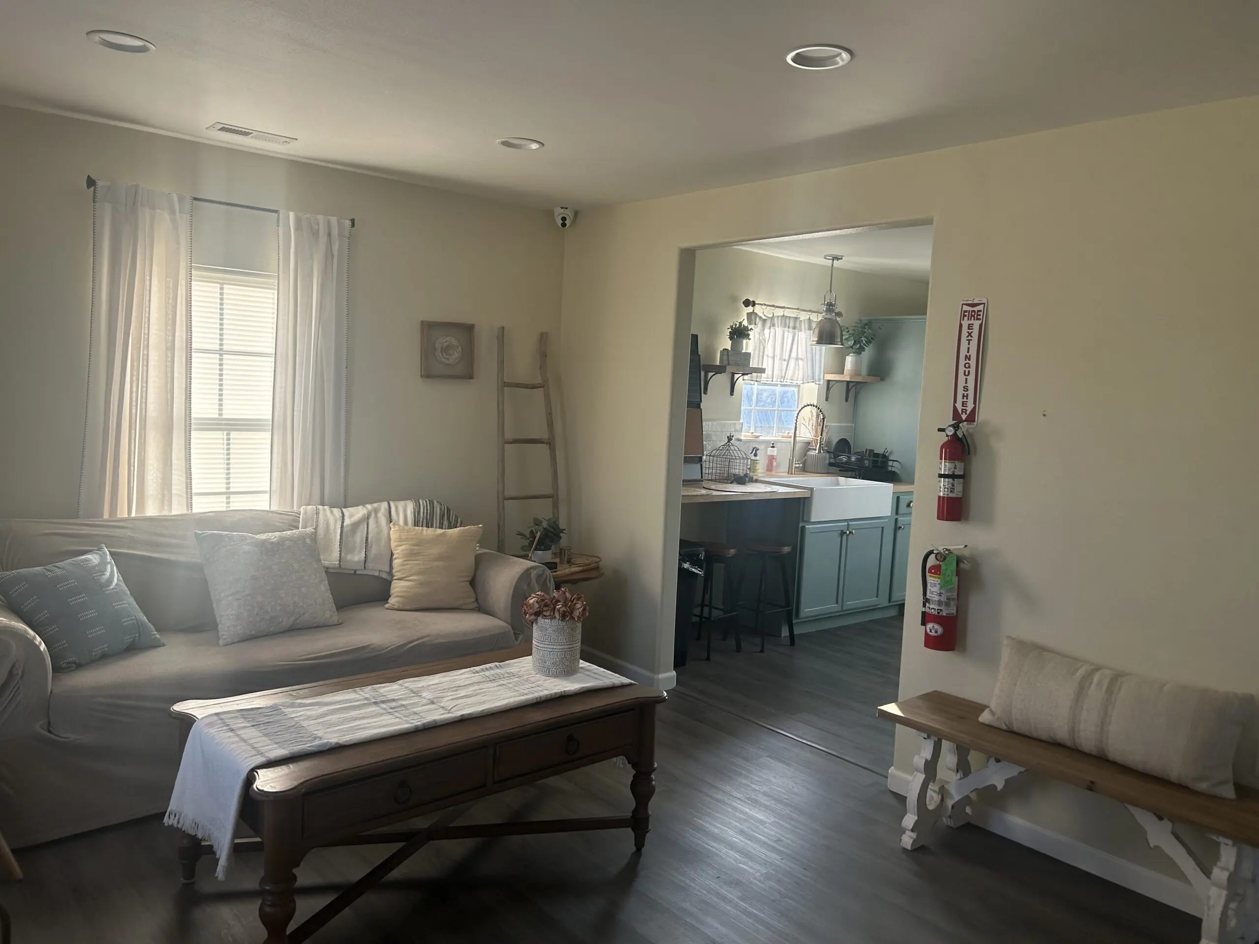 Furnished living room with a gray sofa, wooden coffee table and kitchen visible through an archway