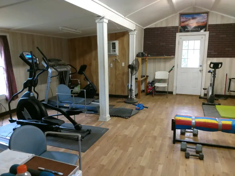 Exercise room with cardio machines, weights, and a Perseverance poster on a brick wall