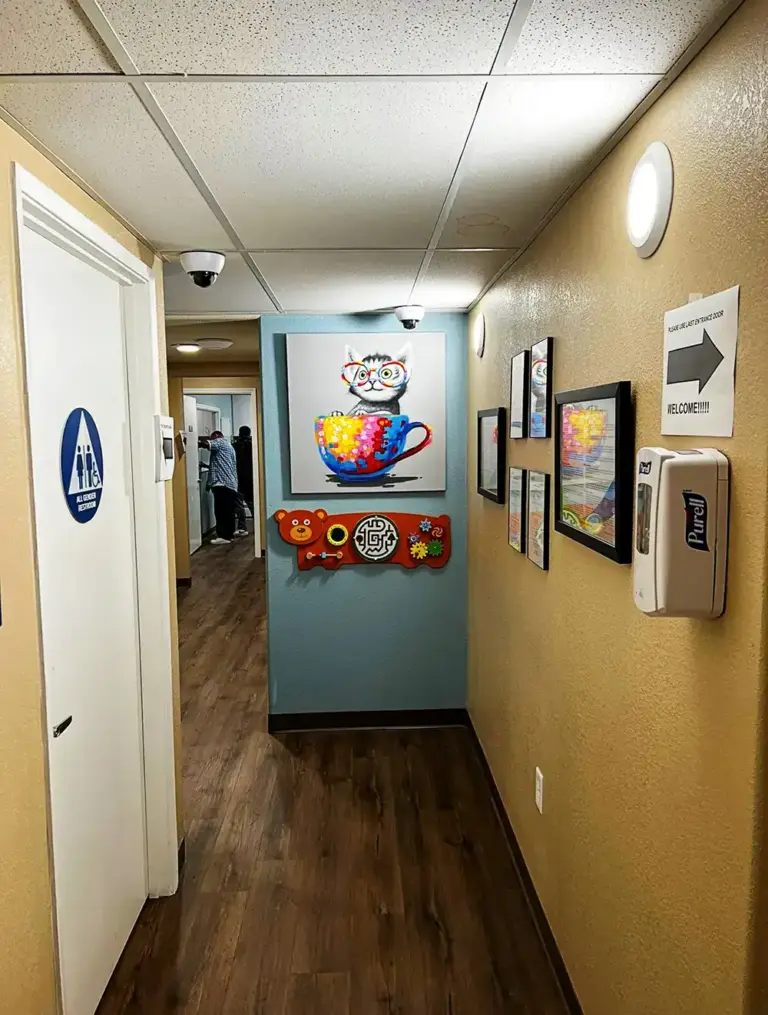 Hallway with wall artwork, an all-gender restroom sign, and a hand sanitizer dispenser
