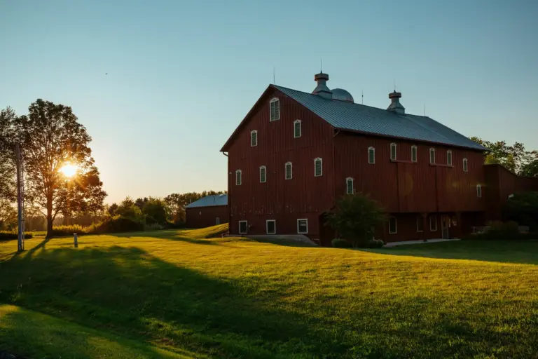Large red barn-style building with a grassy lawn and a low sun in the trees