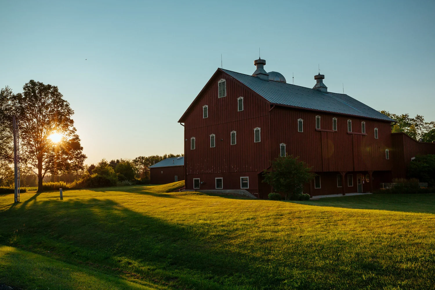 Large red barn-style building with a grassy lawn and a low sun in the trees