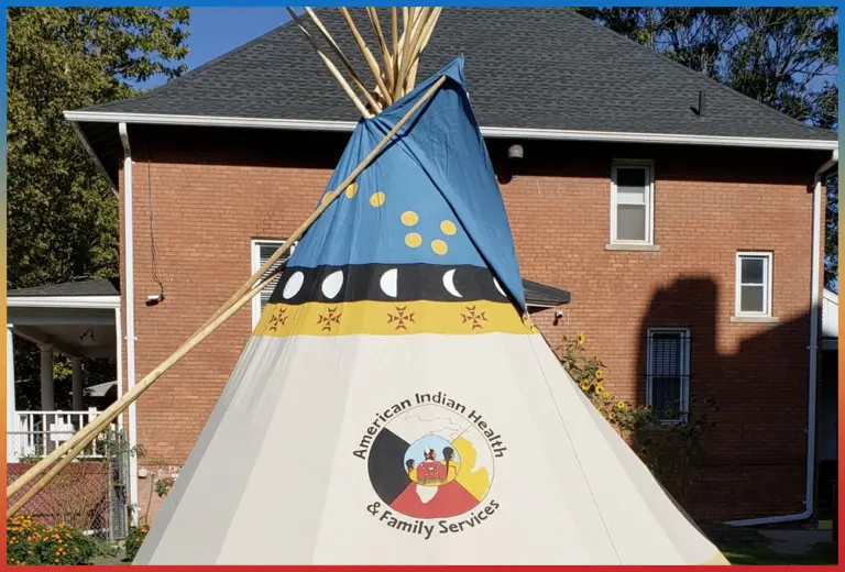 Brick building behind a tipi bearing the American Indian Health & Family Services logo