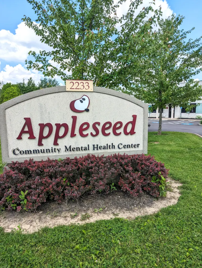 Appleseed Community Mental Health Center sign with address 2233 in front of green shrubs and trees