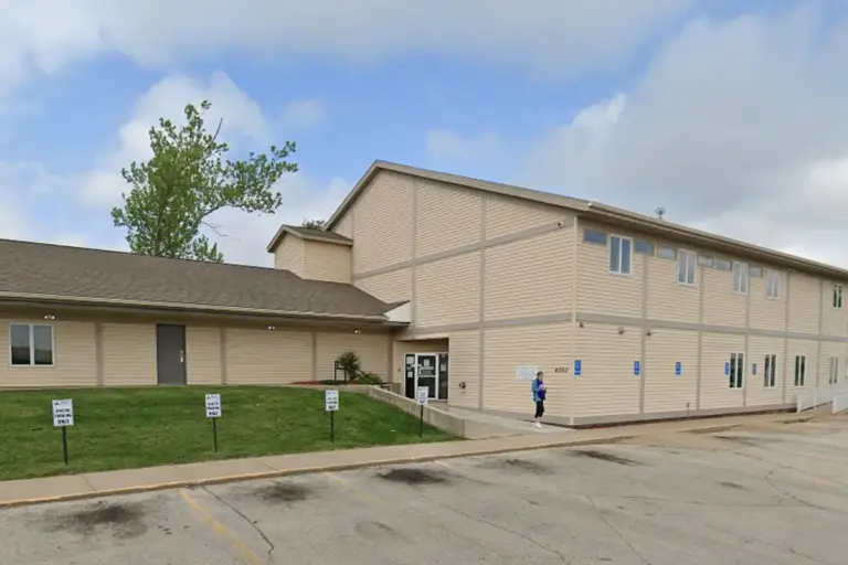 Two-story tan vinyl-sided building with a covered entrance and a parking lot in front