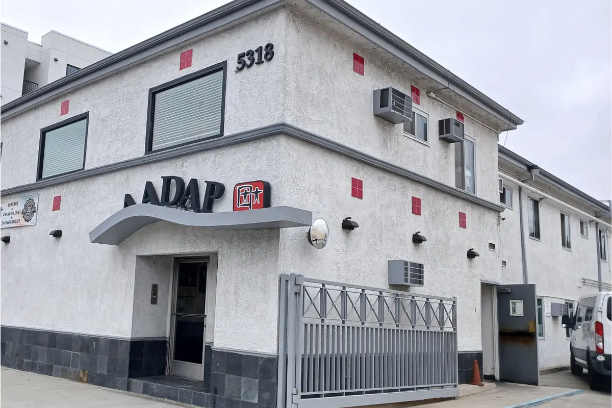 Two-story white stucco building with AADAP sign and red logo, number 5318 above the entrance
