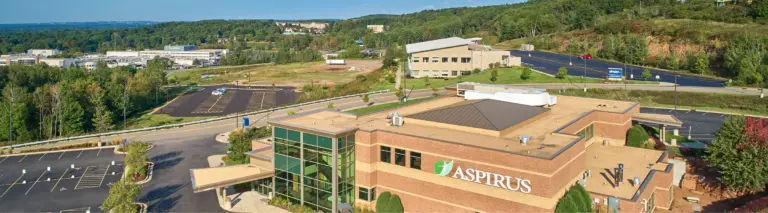 Aerial view of a brick Aspirus building with a glass entrance and surrounding parking lots