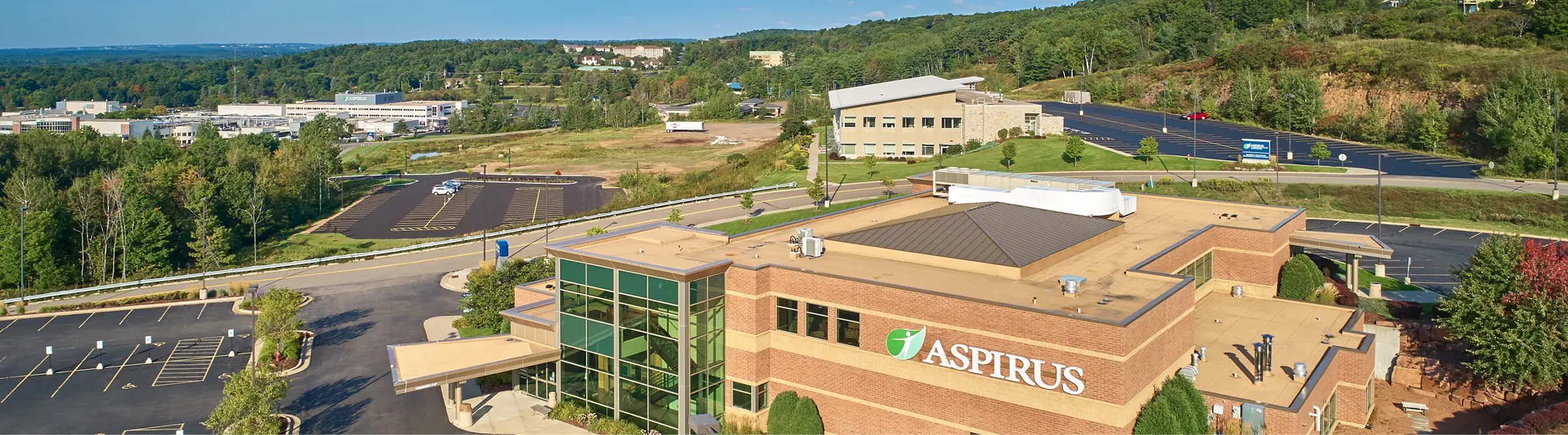 Aerial view of a brick Aspirus building with a glass entrance and surrounding parking lots