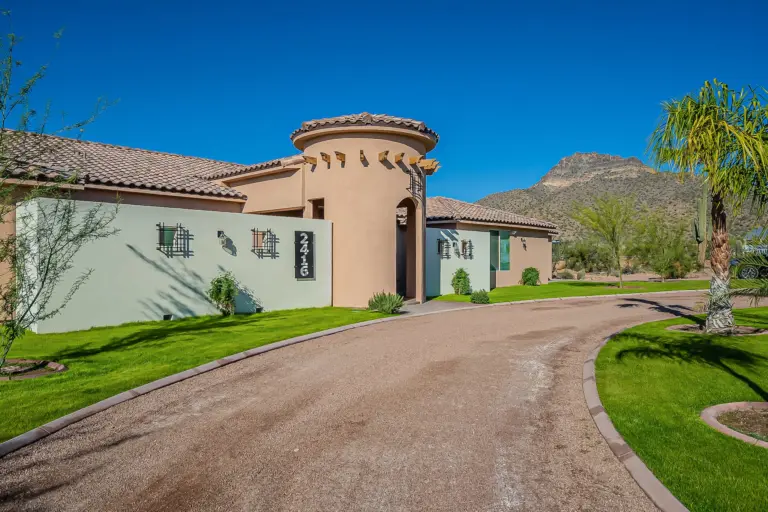Southwestern-style home with stucco walls, tile roof, and a curved gravel drive under a blue sky