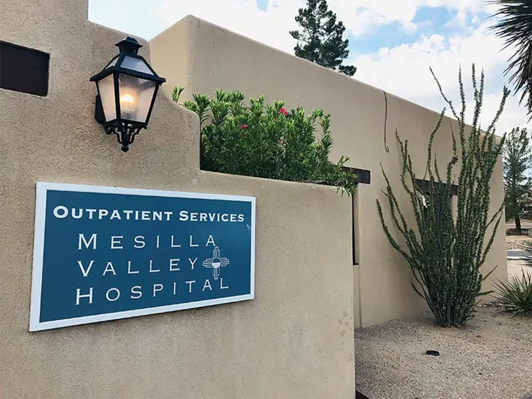 Stucco building entrance with a blue Mesilla Valley Hospital Outpatient Services sign and a lantern