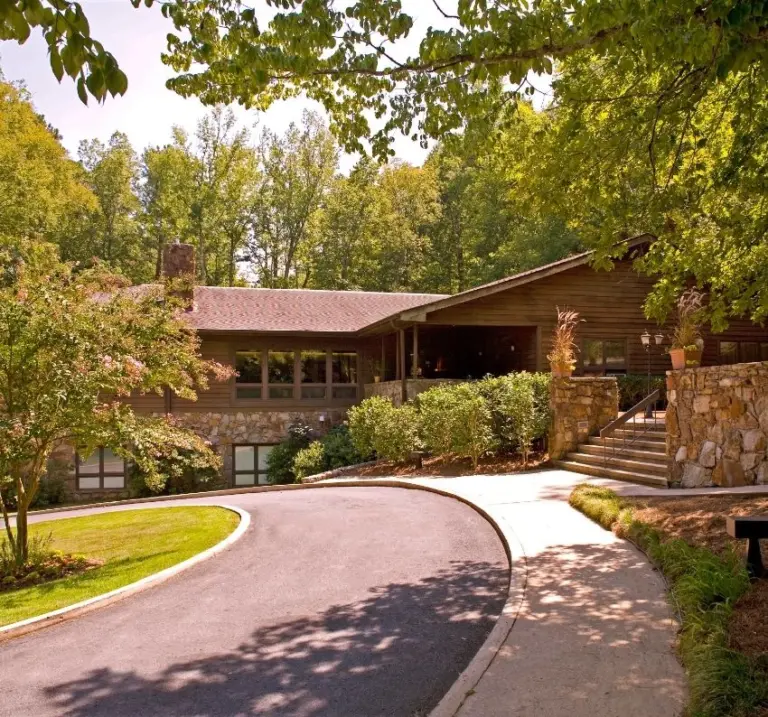 Two-story wood and stone building with a curved driveway and entrance steps among trees
