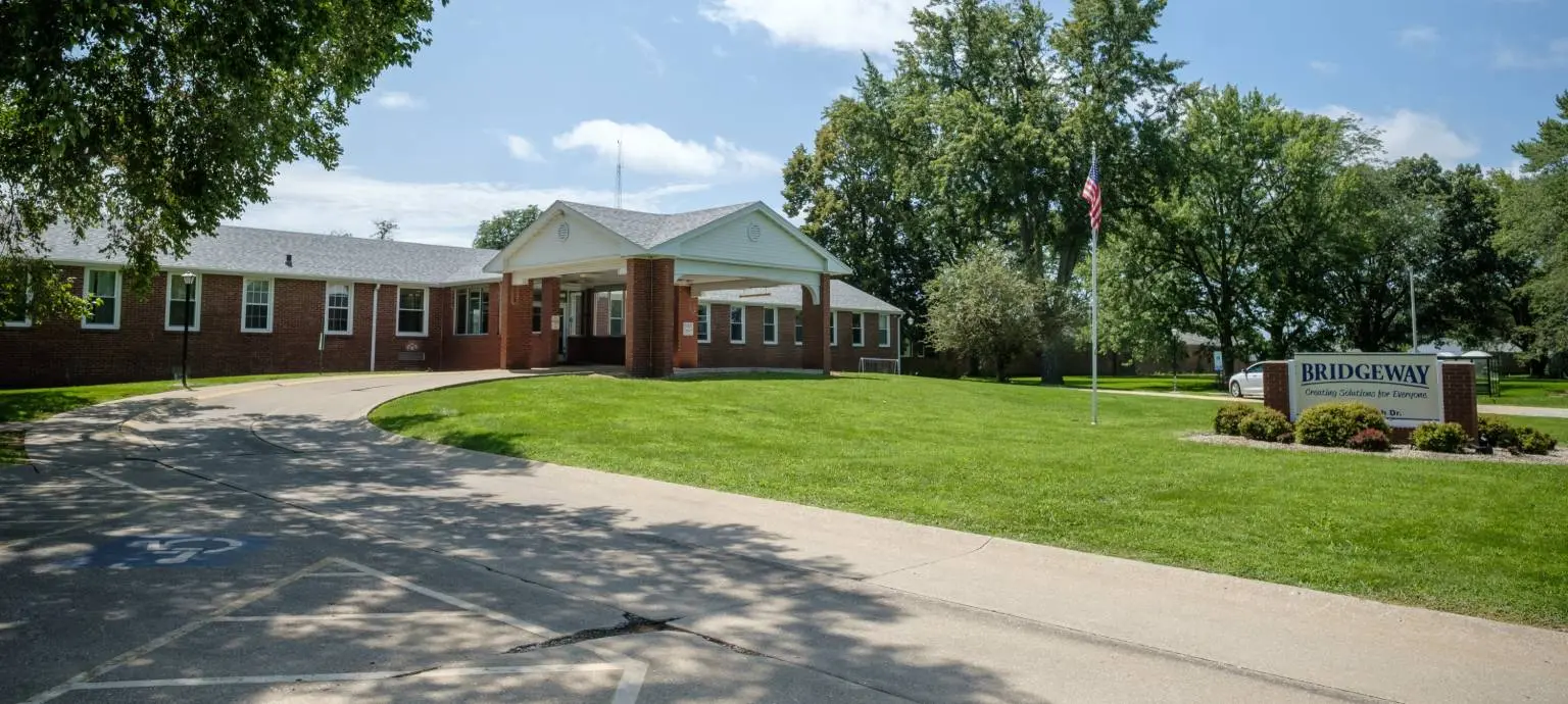 Brick building entrance with a Bridgeway sign and flag on a lawn