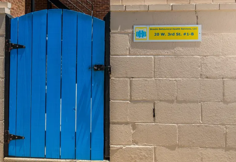 Blue door beside a wall sign reading Brooks Behavioral Health Services, LLC, 20 W. 3rd St. #1-B