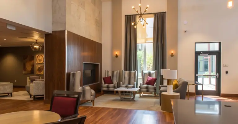 Lounge with wingback armchairs, a fireplace wall, and a glass entry door under tall windows