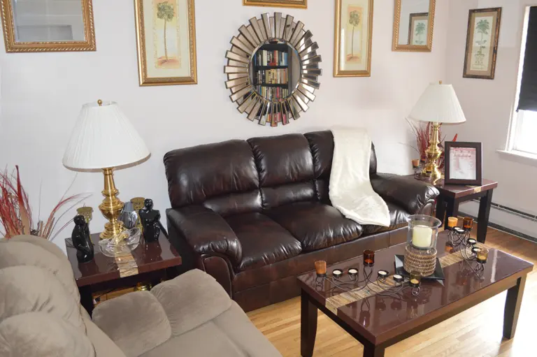 Living room with brown leather sofa, glass-topped coffee table, table lamps and framed palm prints on the wall