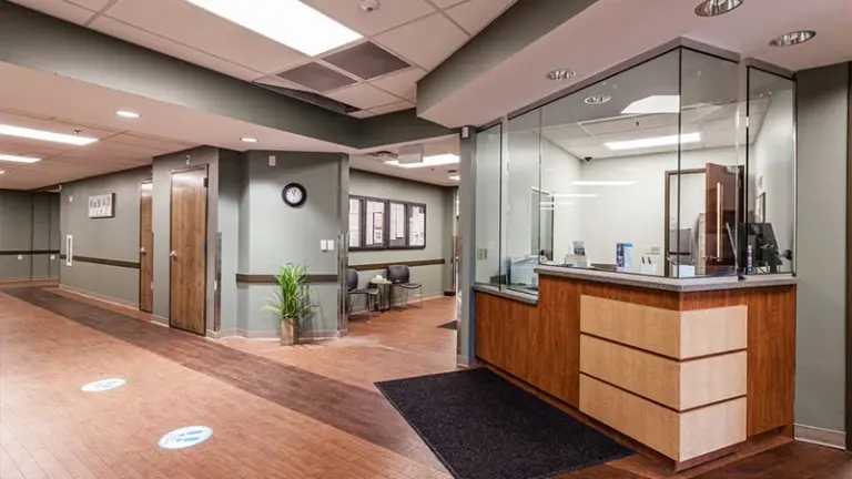 Reception area with glass front desk and wood cabinetry, with hallway and waiting area beyond