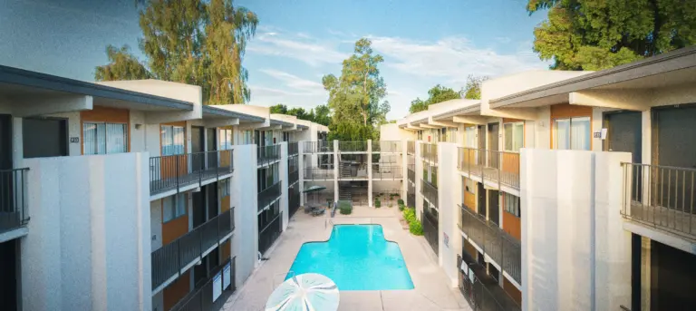 Two-story apartment complex with a central pool and courtyard under a blue sky