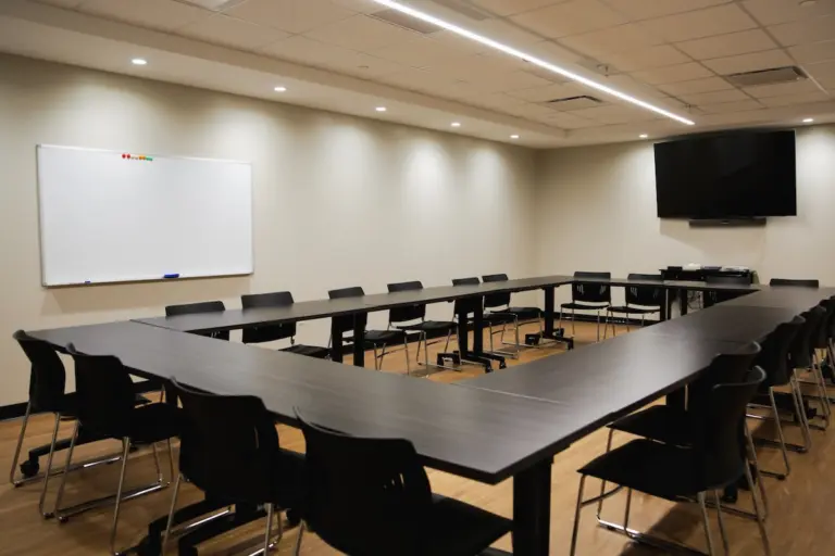 Group room with a U-shaped table, black chairs, a whiteboard and a wall-mounted TV