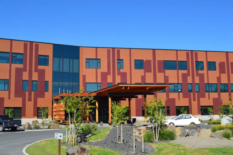Three-story brick-toned building with a wooden covered entrance and landscaped grounds