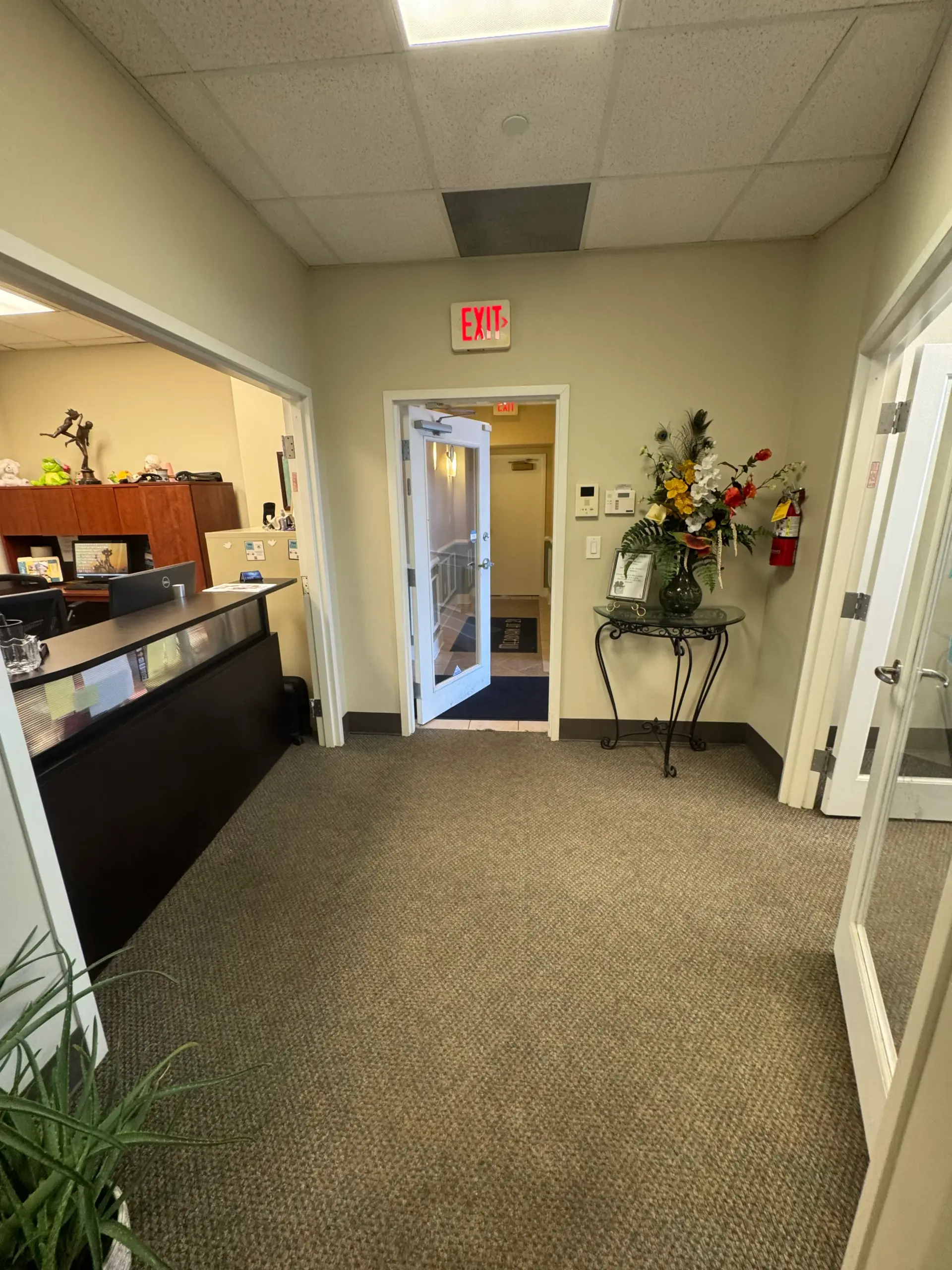Carpeted reception hallway with a front desk, flower arrangement, and glass doors