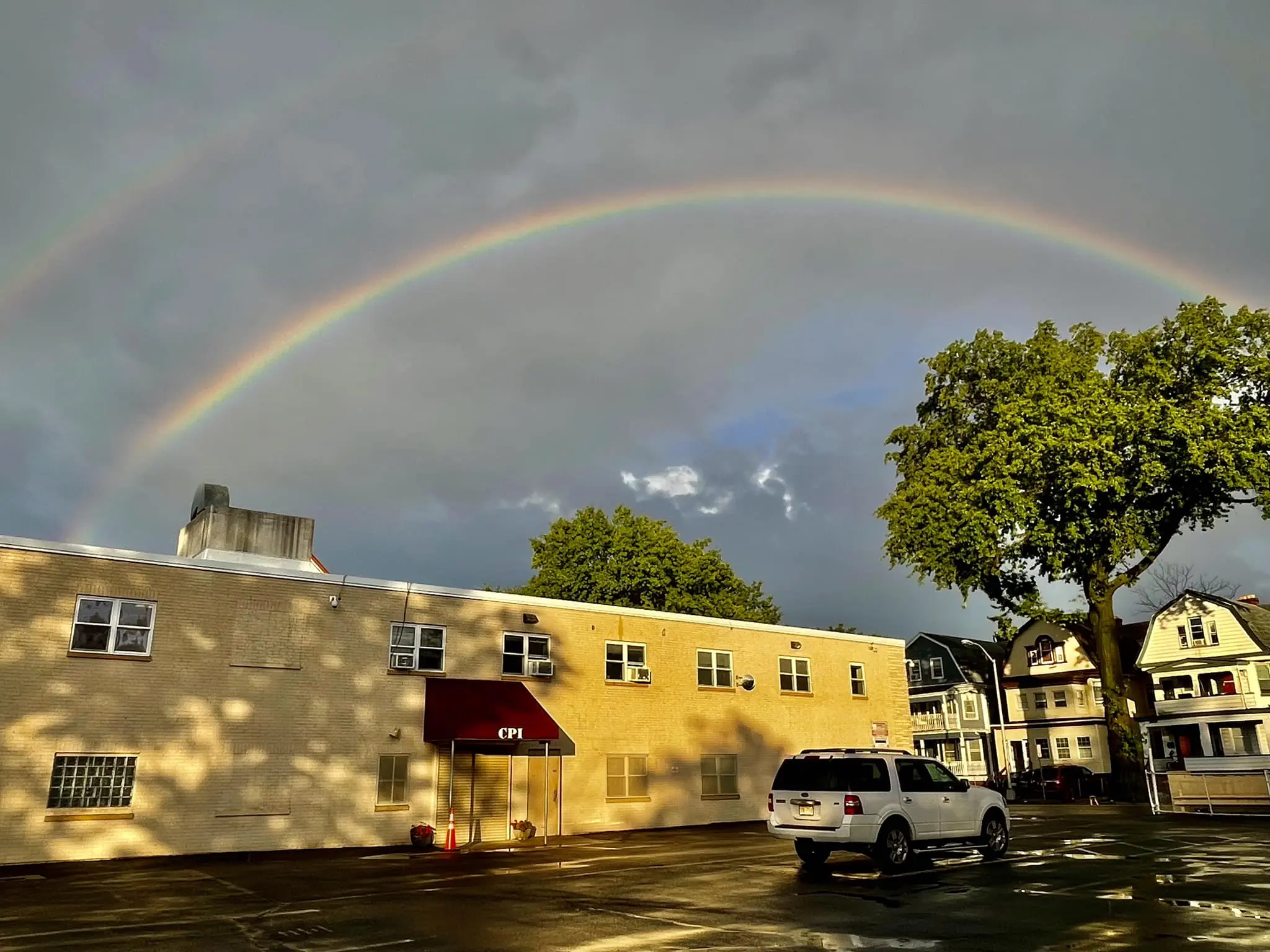 Two-story tan brick building with a red awning marked CPI under a double rainbow