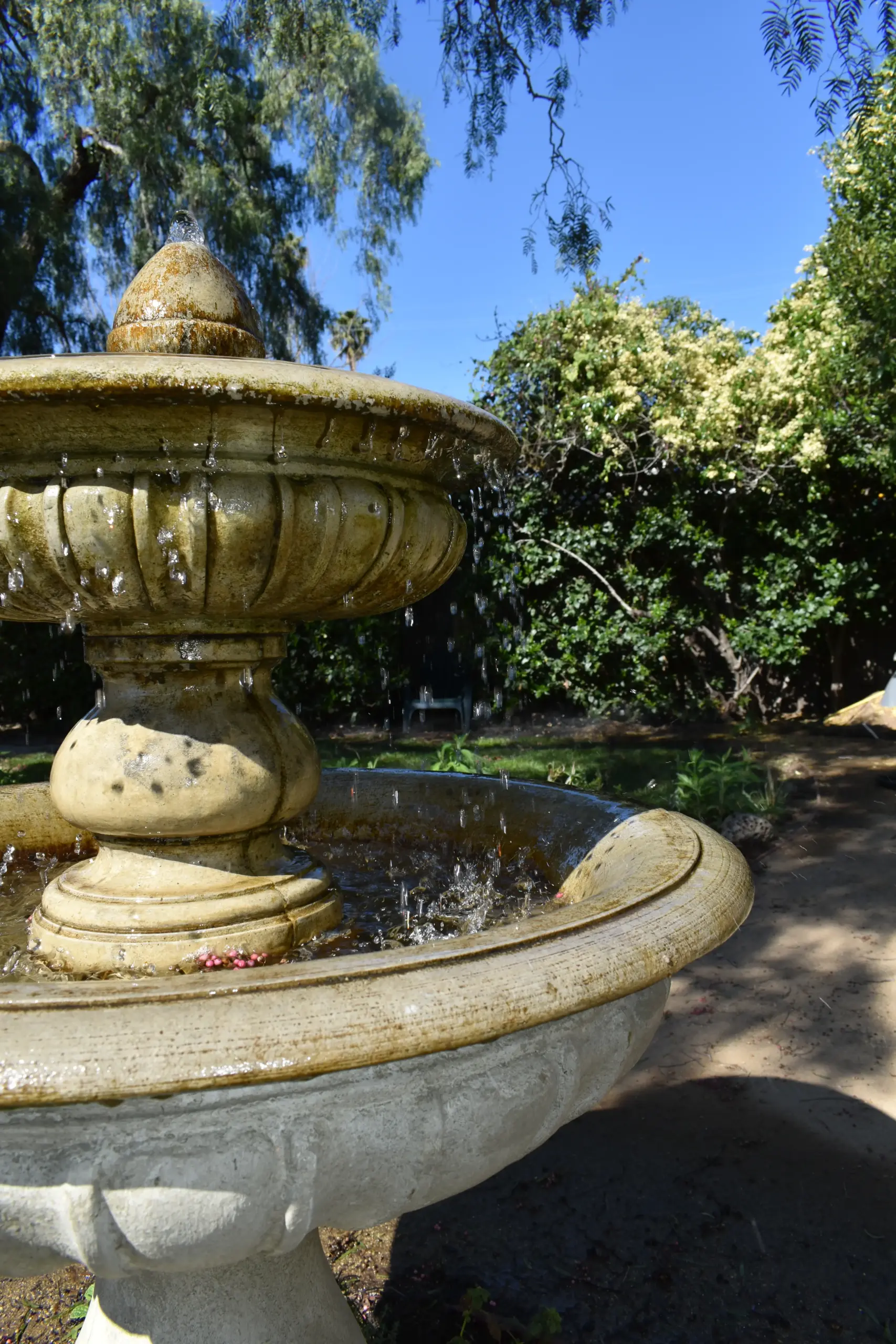 Stone tiered fountain in a garden with trees and a clear blue sky