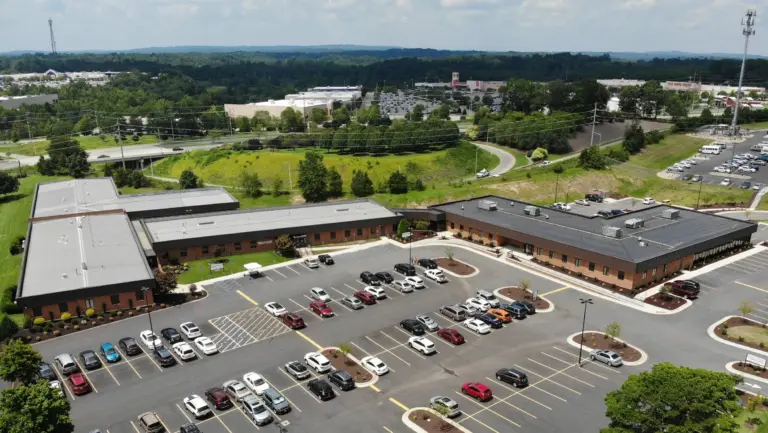 Aerial view of a brick campus with several low buildings, surrounding parking lots, and trees