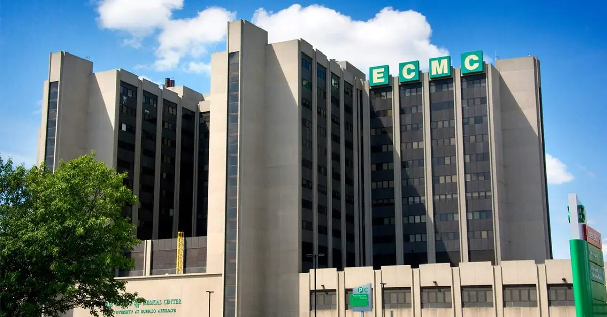 Multi-story concrete hospital building with green ECMC letters on its roof under a blue sky