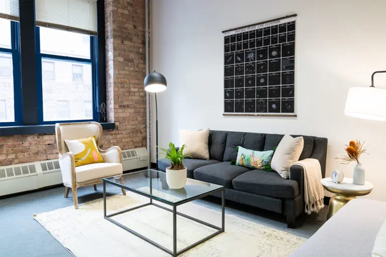 Living room with exposed brick wall, gray sofa, glass coffee table, and a wall poster