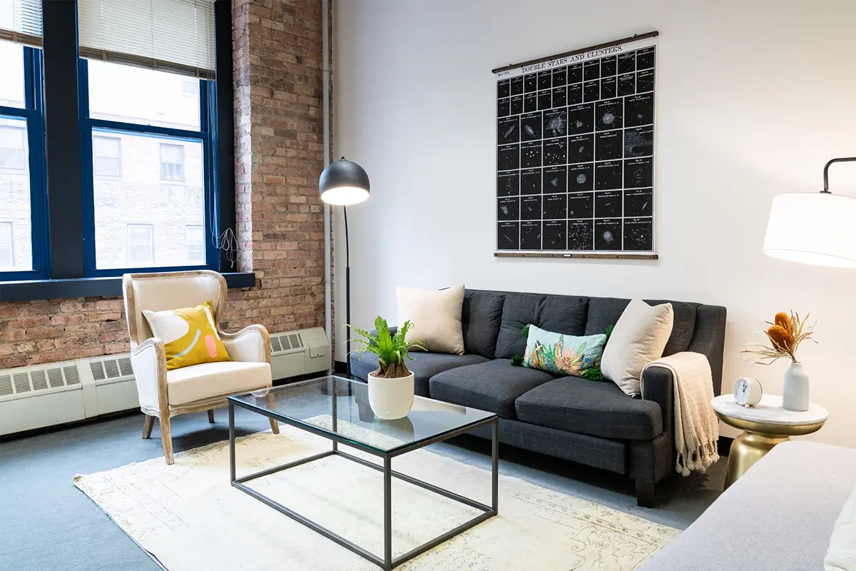 Living room with exposed brick wall, gray sofa, glass coffee table, and a wall poster