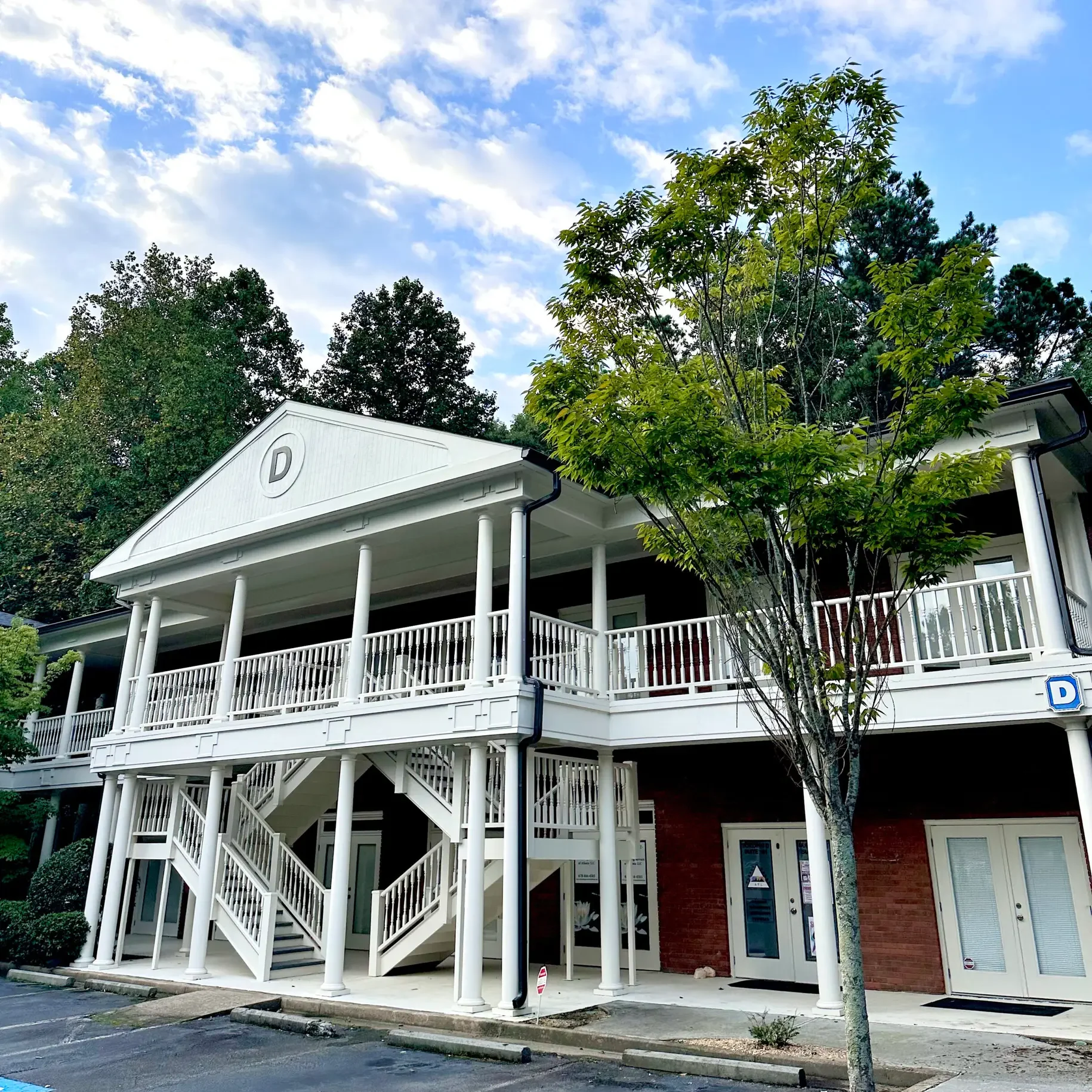 Two-story white-columned building with red brick walls and a trees and parking lot in front