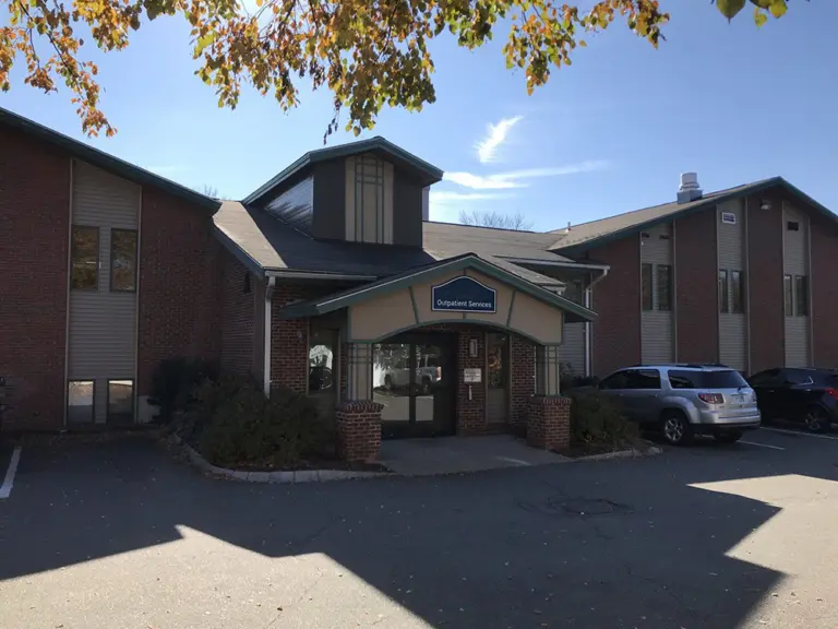 Brick two-story building with an entrance canopy and an Outpatient Services sign, with parking in front