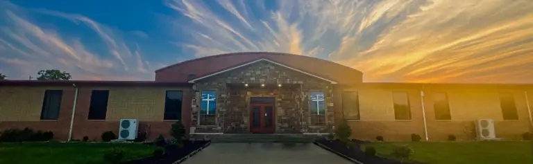 Brick and stone campus building with cross windows and entrance under a sunset sky