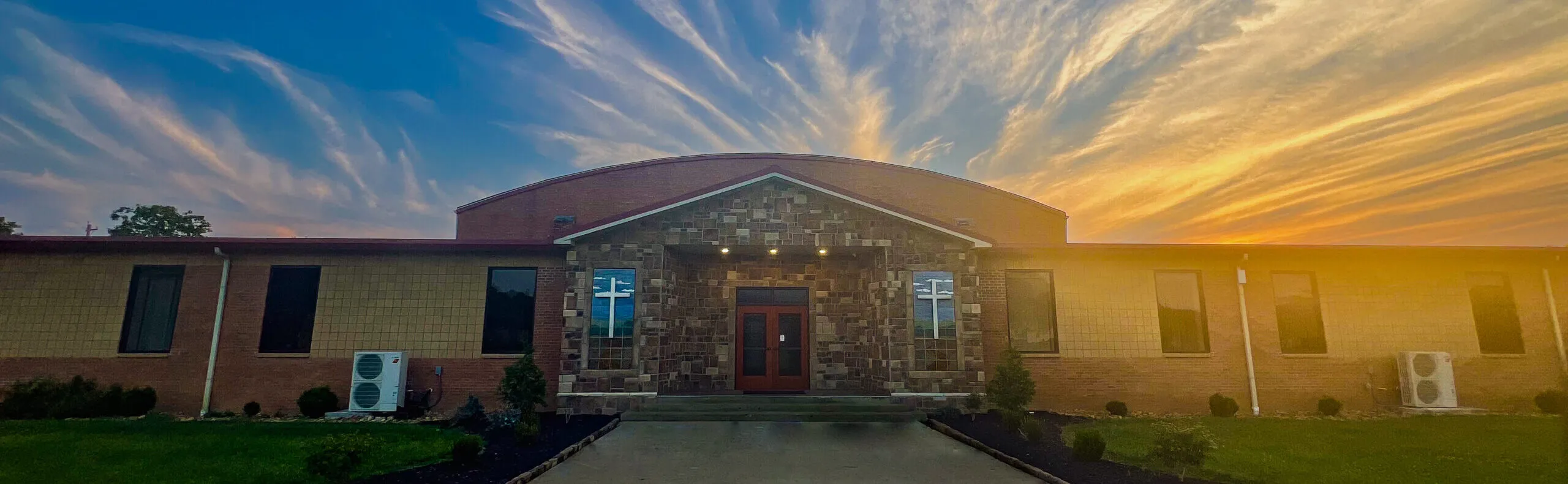 Brick and stone campus building with cross windows and entrance under a sunset sky