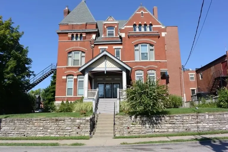 Three-story red brick building with a central entrance and a stone retaining wall in front