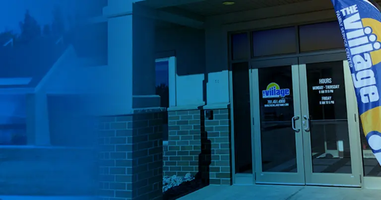 Brick entrance with glass doors and a Village Family Service Center flag, under a blue tint