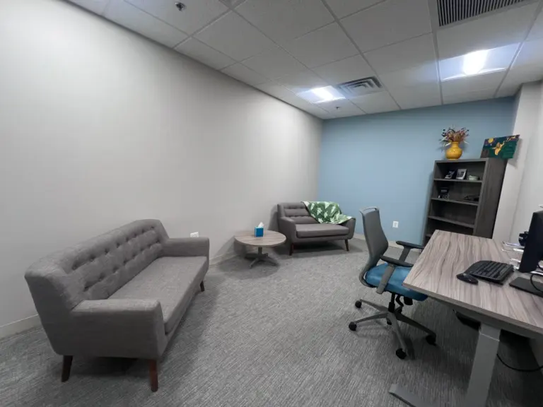 Counseling office with gray sofa, armchairs, side table, and desk with computer
