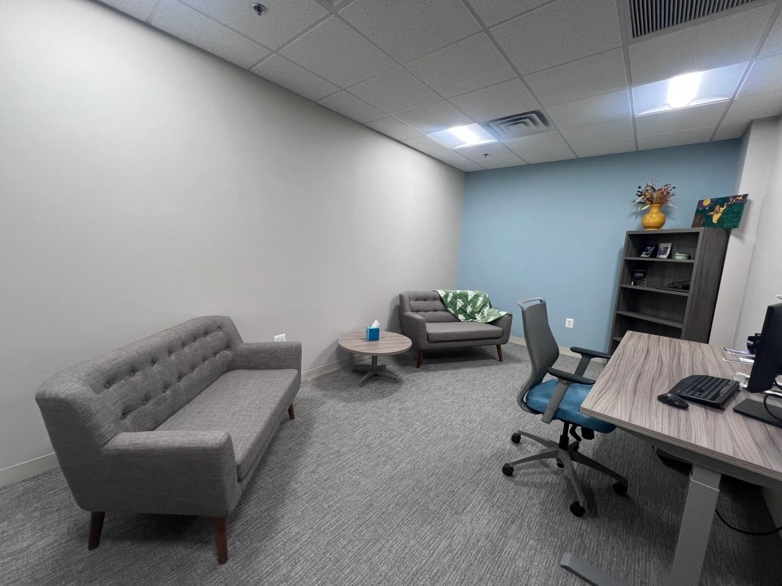 Counseling office with gray sofa, armchairs, side table, and desk with computer
