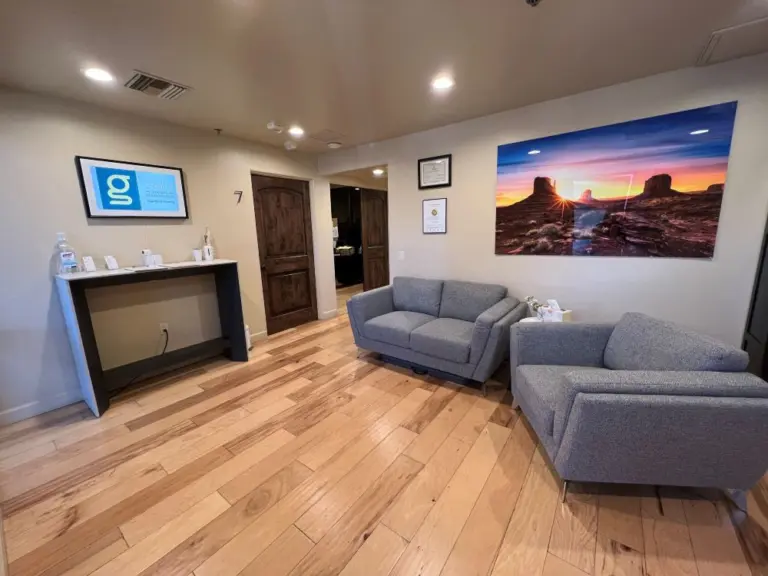 Waiting room with gray sofas, light wood floors, and a desert sunset photo on the wall