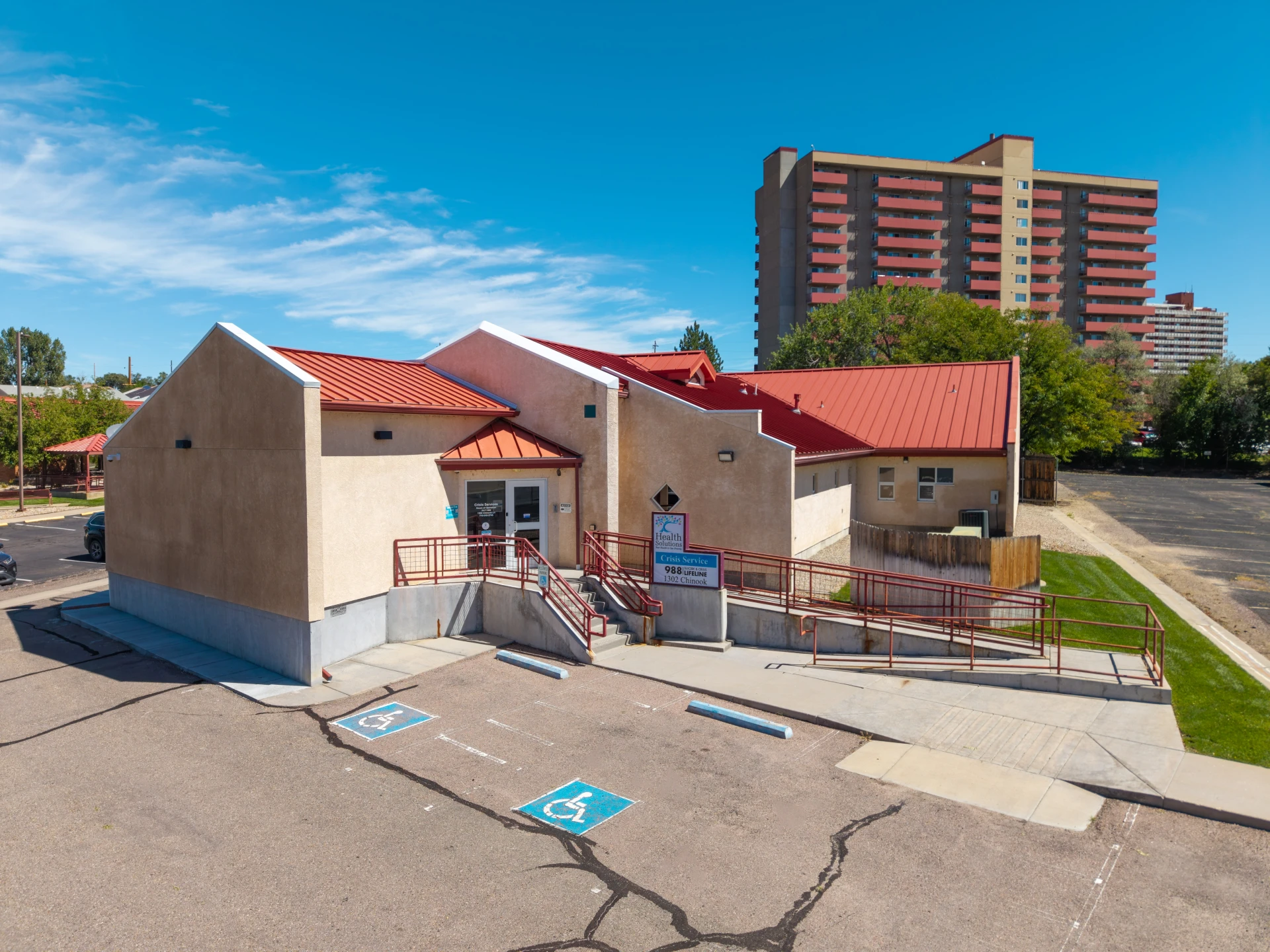 Single-story tan building with red roof and Health Solutions crisis service sign, next to a parking lot