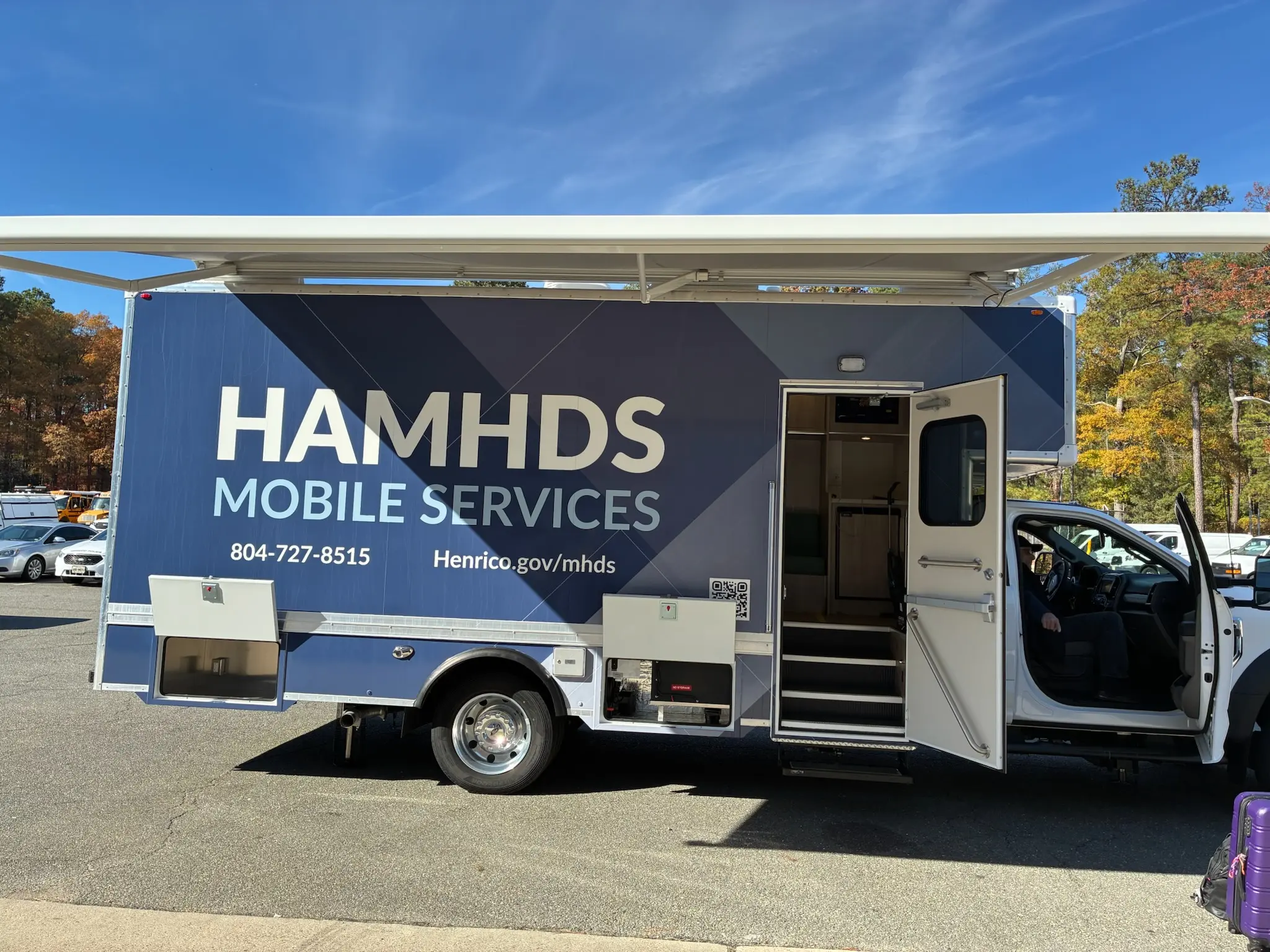 White and navy HAMHDS Mobile Services truck with open side door parked in a lot under blue sky