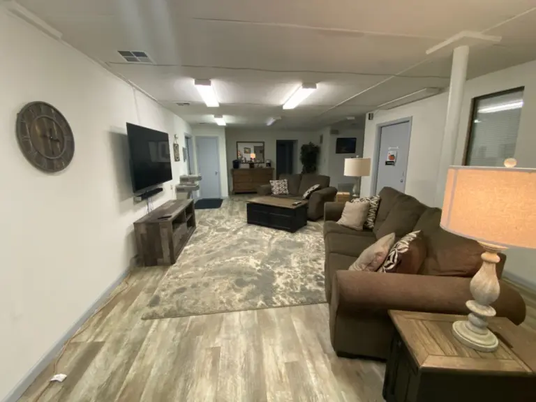 Living room with brown sofas, a wall-mounted TV, and wood-look flooring at a residential treatment facility