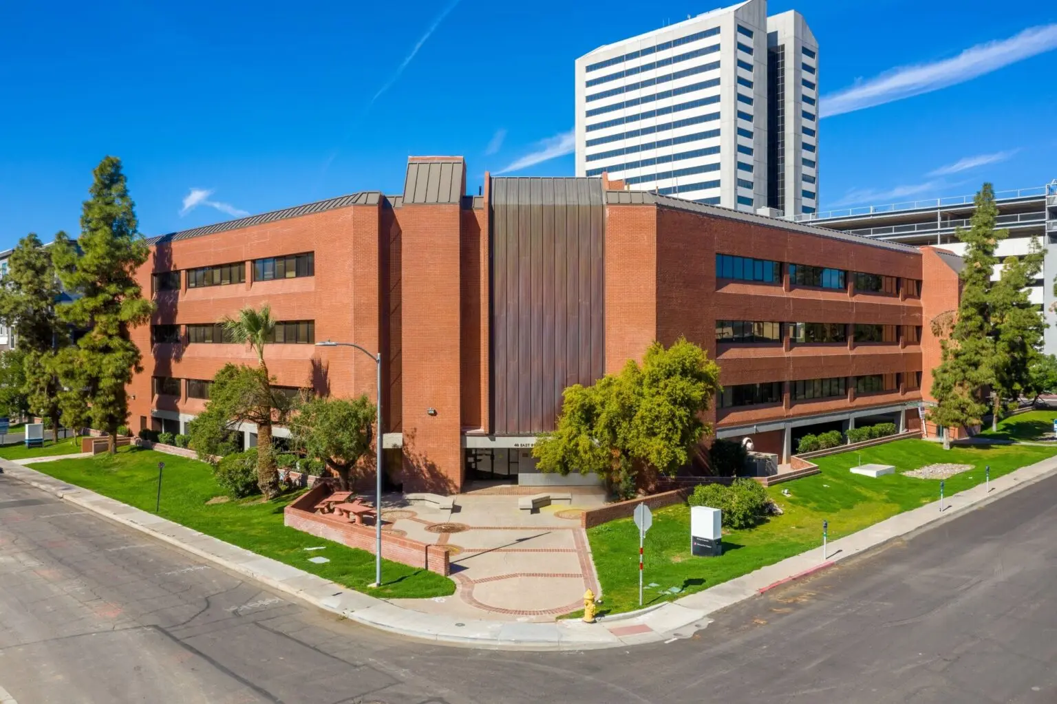 Four-story brick office building with a landscaped entrance courtyard and palm trees under a blue sky