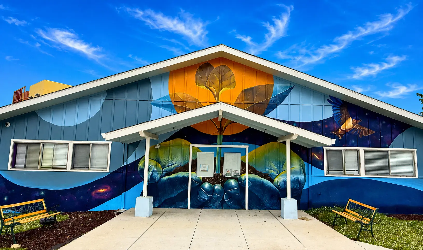 Front entrance of Cronin House, a blue building with a large painted mural of a tree and a flying bird