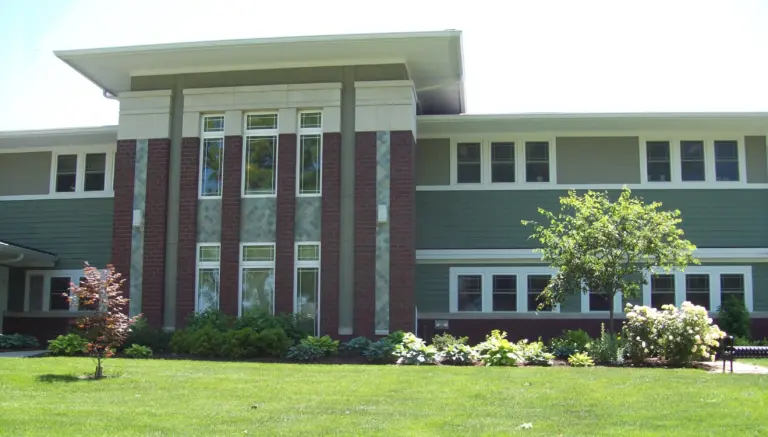 Two-story brick and green-siding building with a lawn and landscaped entrance