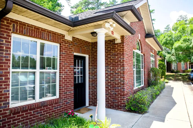 Red brick building entrance with white column, black front door, and sidewalk