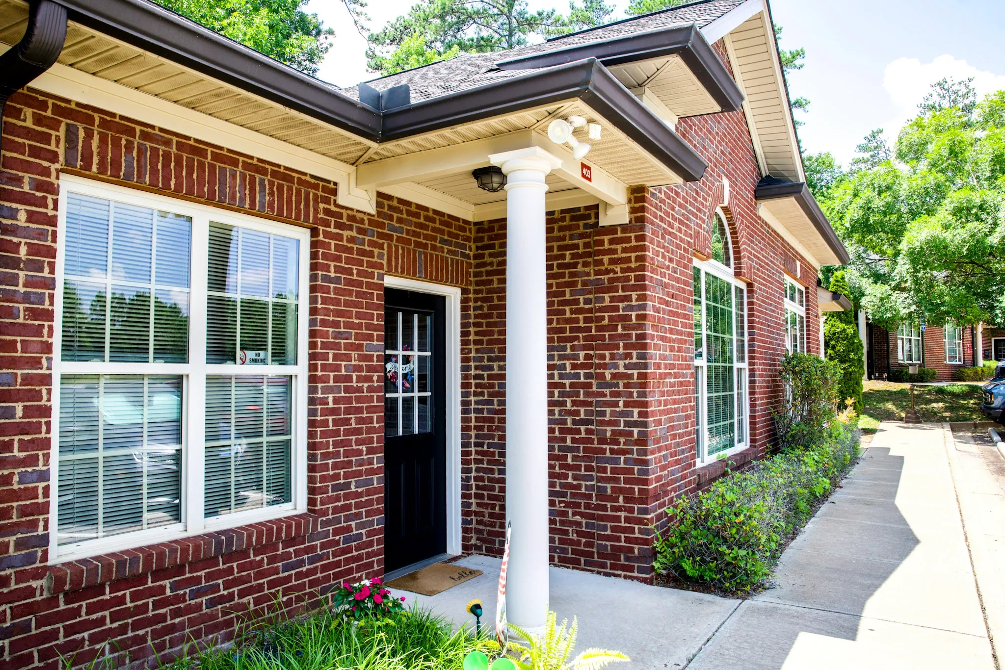Red brick building entrance with white column, black front door, and sidewalk