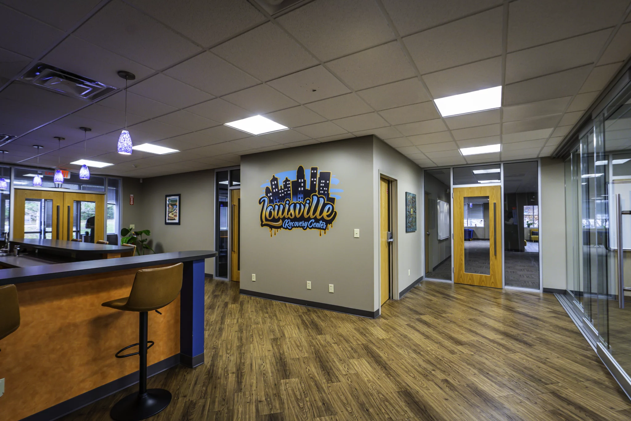 Entry area with a Louisville Recovery Center wall sign, wood-look flooring, and a bar counter with stools