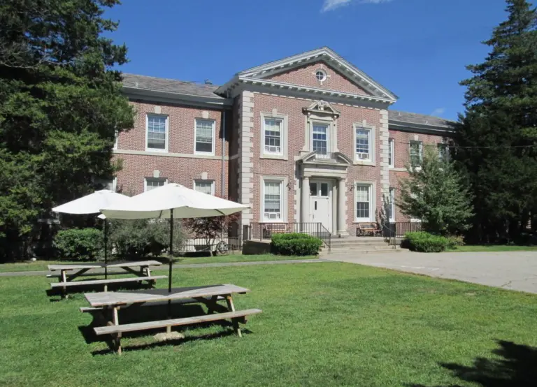 Two-story brick building with a white entrance portico and picnic tables on a lawn