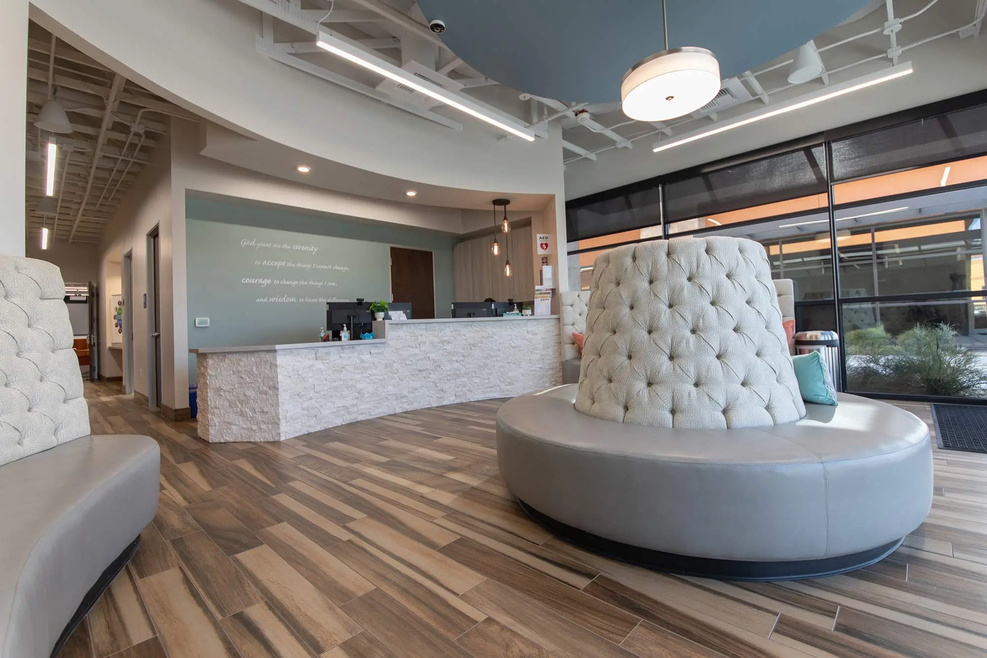 Lobby with tufted gray seating, a stone reception desk, and wood-look floors